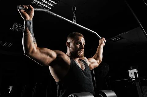 Professional athlete performs an exercise in the gym. Pulls the bar to the .. Stock Photos