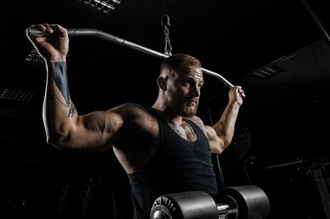 Professional athlete performs an exercise in the gym. Pulls the bar to the .. Stock Photos