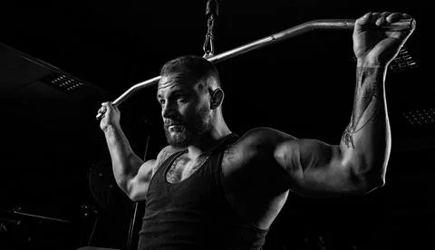 Professional athlete performs an exercise in the gym. Pulls the bar to the .. Stock Photos