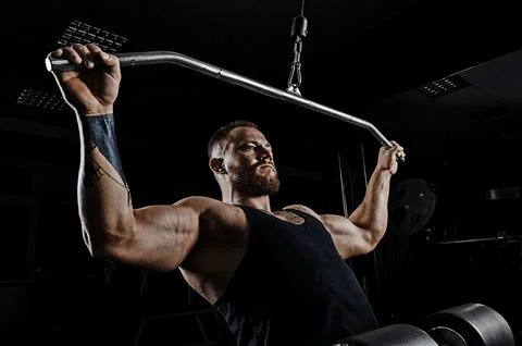Professional athlete performs an exercise in the gym. Pulls the bar to his .. Stock Photos