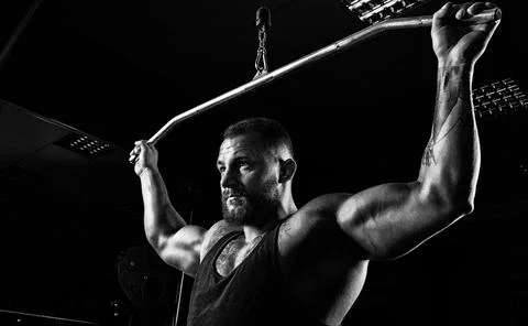 Professional athlete performs an exercise in the gym. Pulls the bar to the .. Stock Photos