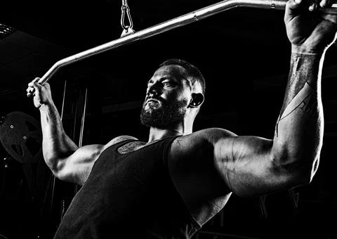 Professional athlete performs an exercise in the gym. Pulls the bar to his .. Stock Photos