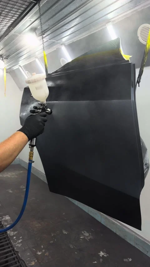 Professional auto body painter applying dark primer to a car door in a spray boo Stock Footage 341134591