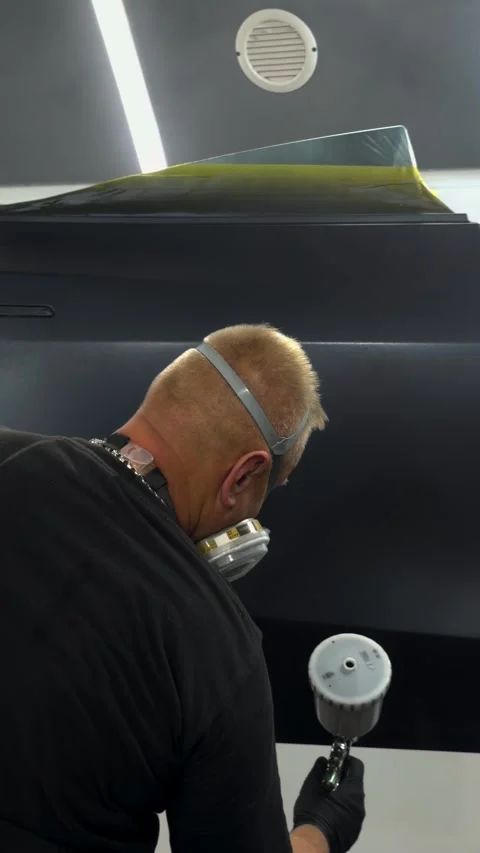 Professional auto body painter applying finish coat in a clean spray booth Stock Footage 341134719