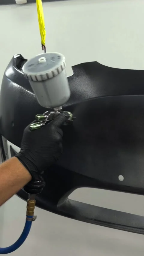 Professional auto body painter applying primer to a car bumper with a spray gun Stock Footage 341134742