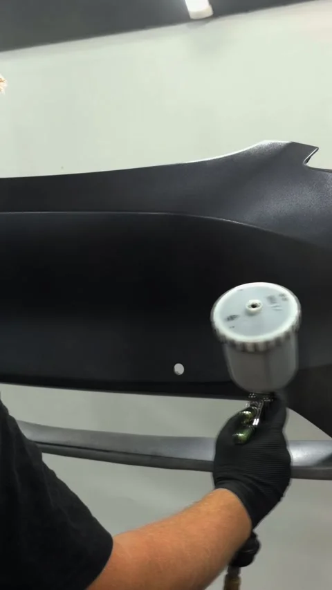 Professional auto body painter applying primer to a car bumper with spray gun Stock Footage 341136115