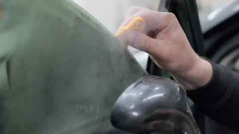 Professional auto service worker carefully removing old tinting film from a car Stock Footage 337537888