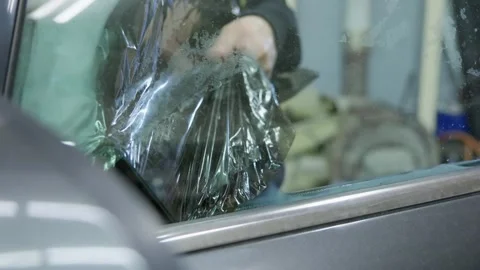 Professional auto service worker carefully peeling off the old tinting film from Stock Footage 337537898