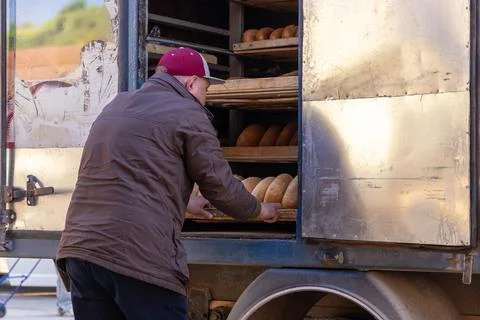 A professional baker is loading freshly baked loaves of rustic bread into a.. Stock Photos