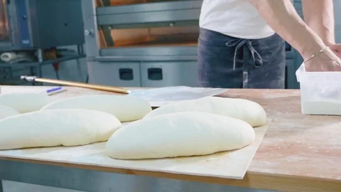 Professional baker pouring a flour on raw bread before baking at bakery kitchen Stock Footage 91124664