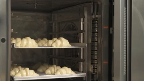 A professional baker putting a tray full of croissants into the oven for baking. 스톡 동영상 107465492