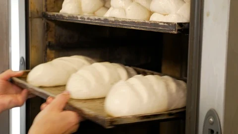 A professional baker putting a tray full of bread into the oven for baking. Stock Footage 108098586