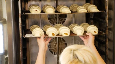 A professional baker putting a tray full of croissants in a large oven Stock Footage 108635055