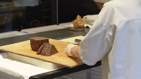 Professional Baker Slicing Dark Rye Bread with Seeds. Chef slicing a triang.. Видео 331213591