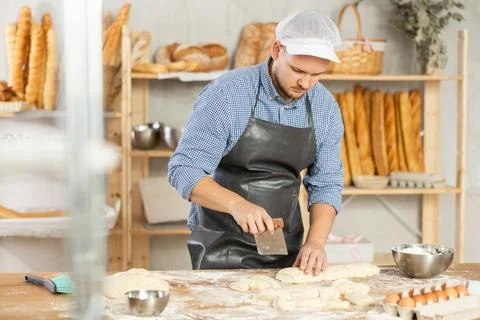 Professional baker uses knife to cut raw dough to make croissants or buns Stock Photos