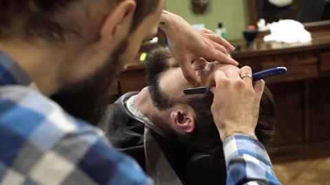 Professional barber shave client's beard with straight razor. very concentrated Stock Footage 69990645