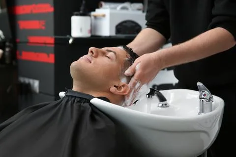 Professional barber washing client's hair at sink in salon, closeup Stock Photos