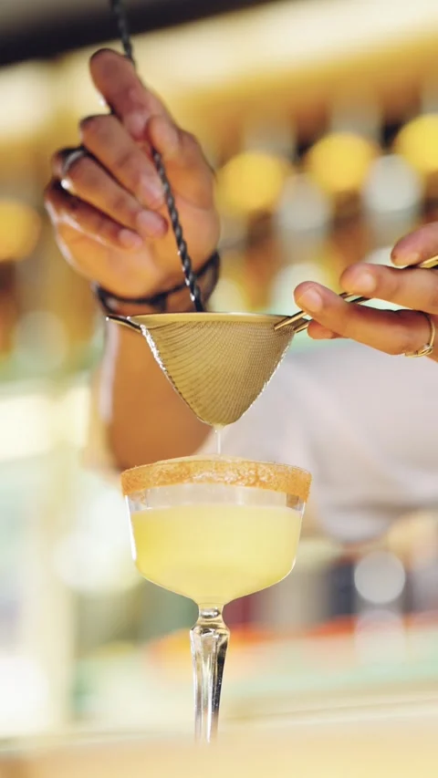 Professional bartender double straining a yellow cocktail Stock Footage 331223227