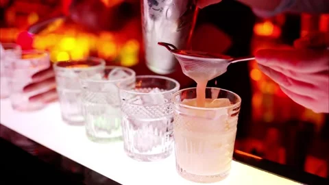 Professional bartender expertly strains and pours cocktails into glasses, d.. Stock Footage 339425073