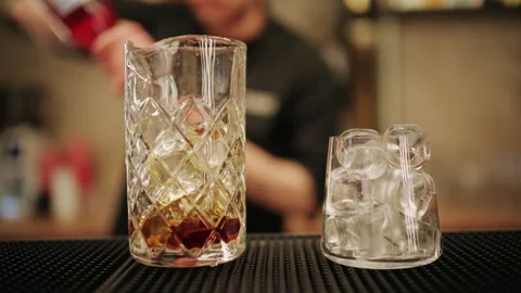 Professional bartender pouring liquor into a mixing glass with ice cubes Stock Footage 332664237