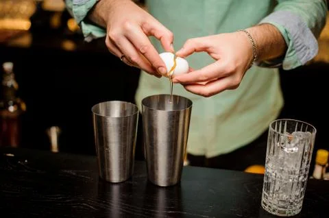Professional bartender at work in bar pouring egg yolk into glass for drink. Photos