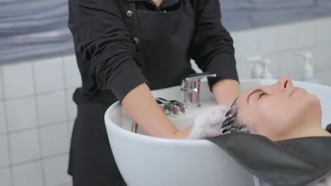 A professional beauty salon worker washing her hair. Clean with shampoo and m Stock Footage 153881053