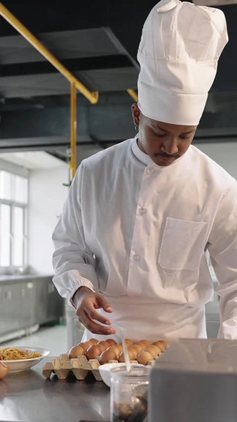 Professional Black chef checking eggs in a bright kitchen, focused on Stock Footage 321929758