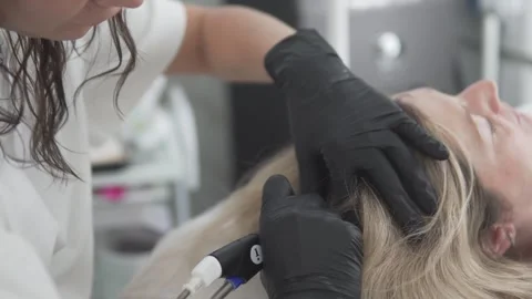 A professional in black gloves performs a scalp care procedure using a special Stock Footage 311871978
