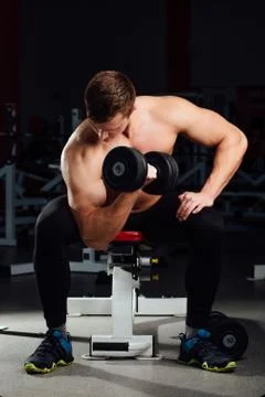 Professional bodybuilder do exercises for biceps sitting on the bench, with Stock Photos