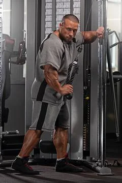 Professional bodybuilder executes a cable exercise in a well equipped gym Stock Photos