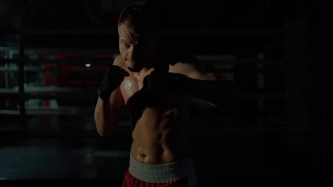 Professional boxer is working out in dark gymnastic hall, hitting in front Video stock 98744222