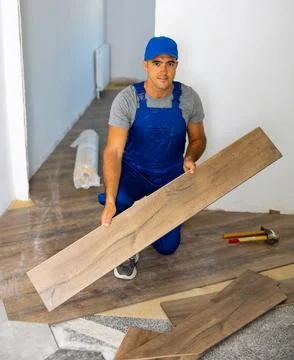Professional builder in blue construction overalls installing wooden laminate Stock Photos