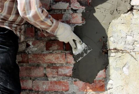 A professional builder bricklayer with hand trowel applies cement mortar to the Stock Photos