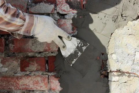 A professional builder bricklayer with hand trowel applies cement mortar to t Stock Photos