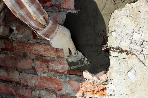 A professional builder bricklayer with hand trowel applies cement mortar t... Stock Photos