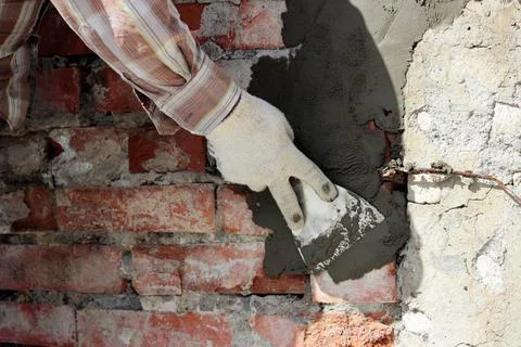 A professional builder bricklayer with hand trowel applies cement mortar t... Stock Photos