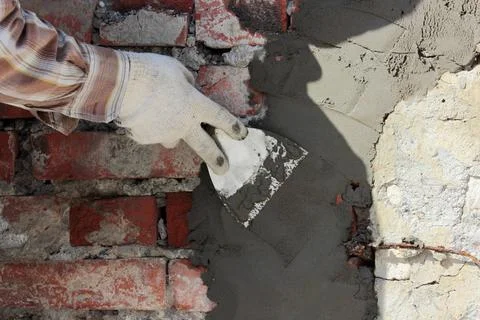 A professional builder bricklayer with hand trowel applies cement mortar t... Stock Photos