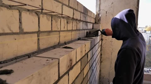 Professional builder in a hood and protective gloves is laying bricks while buil Stock Footage 270519052