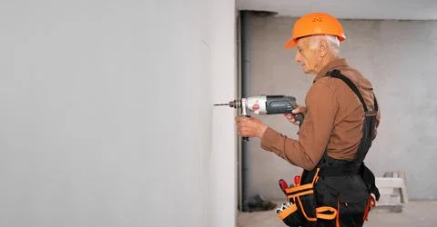 Professional builder or handyman in hardhat using a drill drilling hole in th Stock Photos