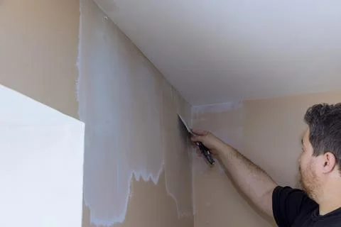 Professional builder smooths wall with spatula putty put on leveled surface o Stock Photos
