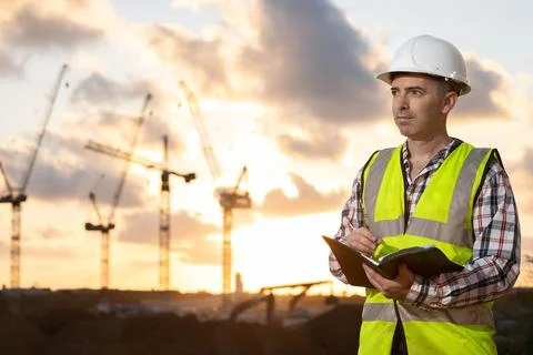 Professional builder standing with a notebook in front of the construction site Stock Photos