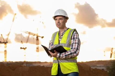 Professional builder standing with a notebook in front of the construction site Stock Photos