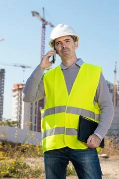 Professional builder standing talking on a phone in front of the constructi.. Stock Photos