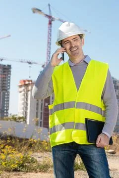 Professional builder standing talking on a phone in front of the constructi.. Stock Photos
