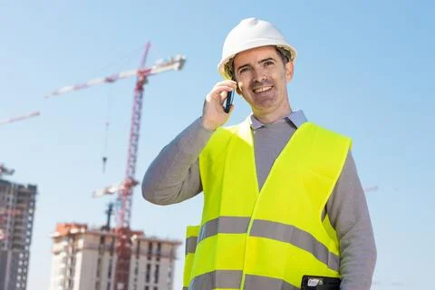 Professional builder standing talking on a phone in front of the constructi.. Stock Photos