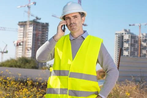 Professional builder standing talking on a phone in front of the constructi.. Stock Photos