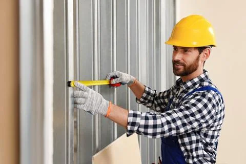 Professional builder in uniform working with measuring tape indoors Stock Photos