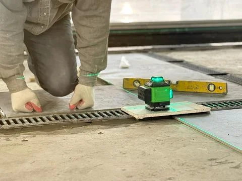 Professional builder worker installing floor a large ceramic tile using a l.. Stock Photos