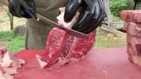 Professional Butcher Cutting Thick T-Bone Beef Steaks on a Red Cutting Board Out Stock Footage 338213048