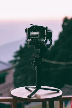 A professional camera gimbal stabilizer stands on a small wooden table during Stock Photos